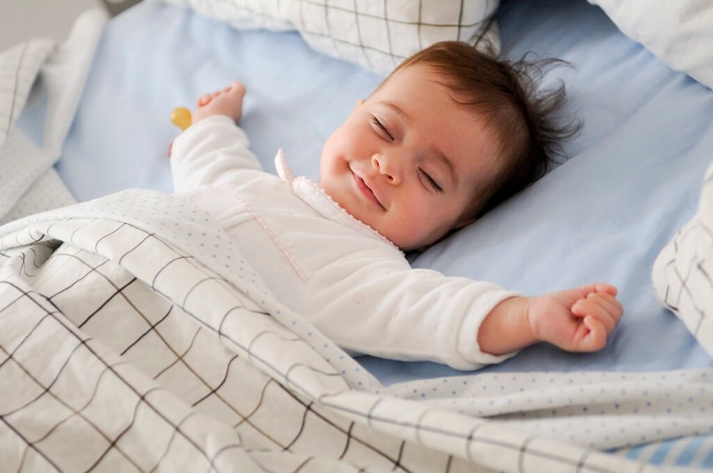 Smiling baby girl lying on a bed sleeping on blue sheets Meditation for Sleep and Anxiety