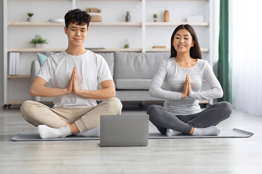 Relaxed asian family practicing morning meditation at home, using laptop meditation videos 1