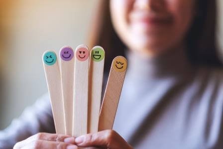 A woman holding colorful hand draw happy emotion faces on wooden stick how to calm down when angry 3