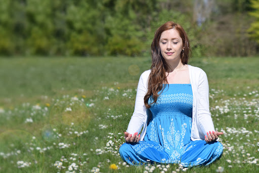 a woman in blue meditating in sunlit grass