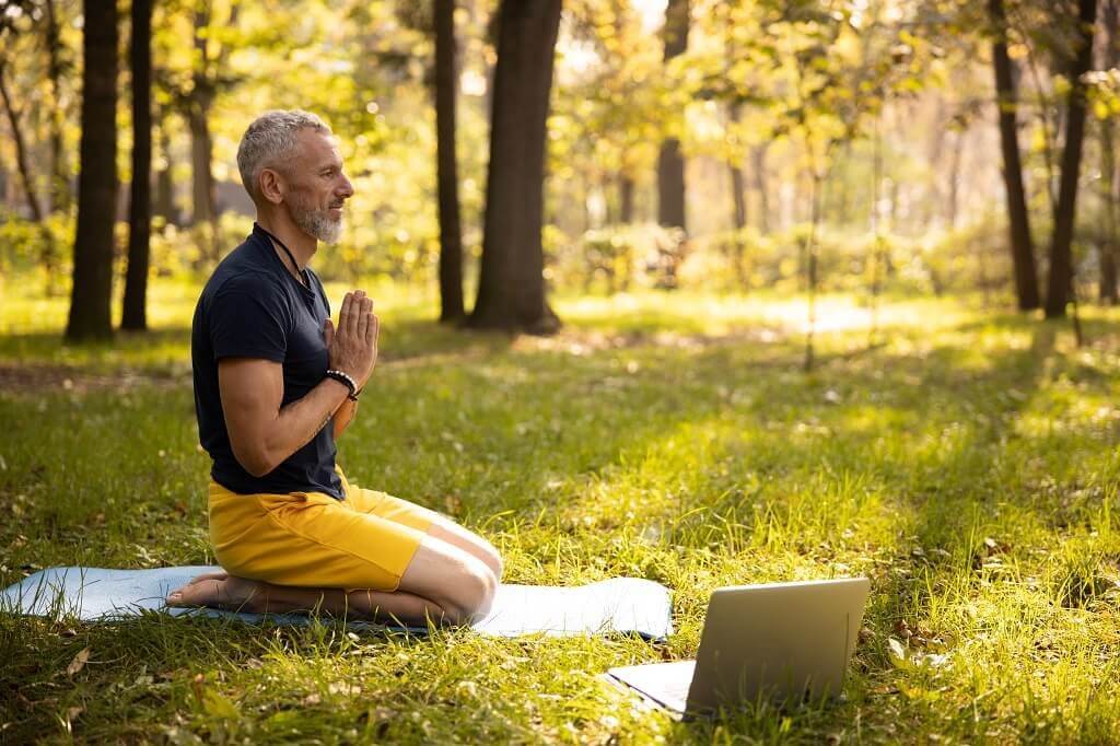 A man participating in an online meditation class in the woods.