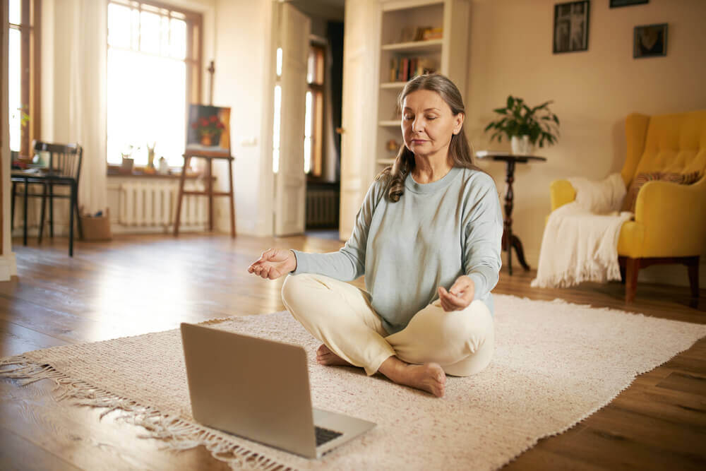 An elderly woman participating in an online meditation course at home.