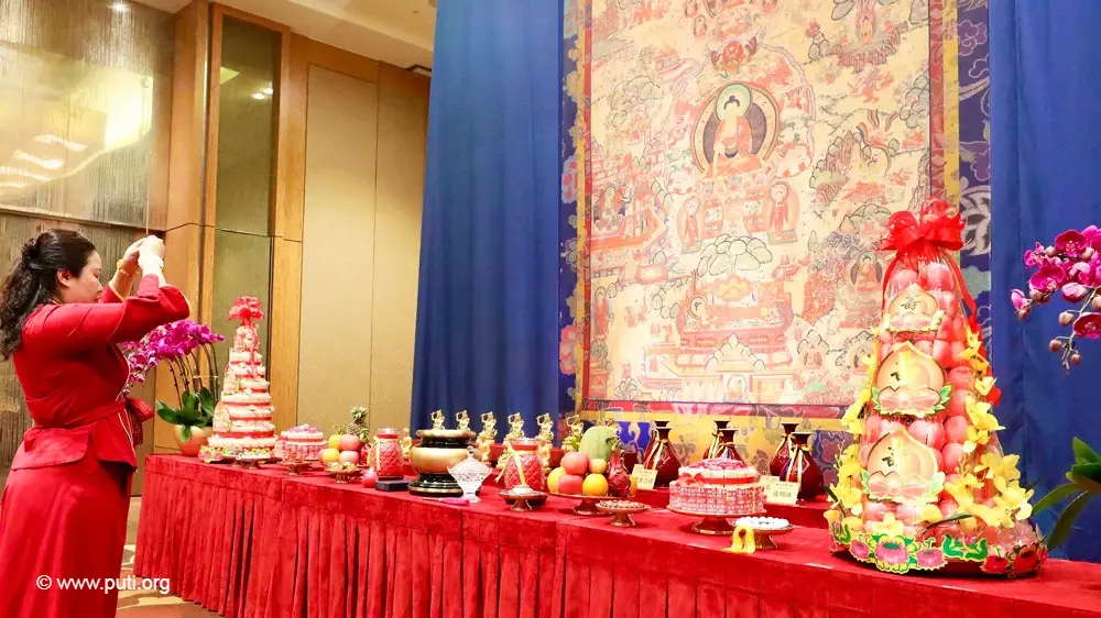 A woman holding incense and worshiping reverently in front of a thangka.