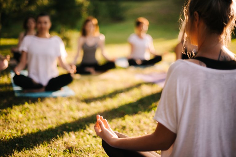 Group of young sporty woman practicing yoga lesson with instructor, sitting in lotus pose.